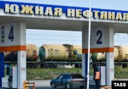 Заправка автомобиля на автозаправочной станции "Южной нефтяной компании". На дальнем плане - железнодорожные цистерны для транспортировки нефтепродуктов. Россия, Краснодар. Иллюстрационное фото