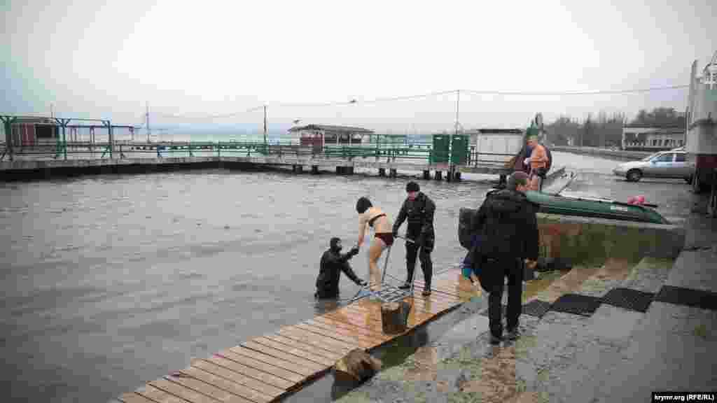 Водолаз помогает девушке зайти в воду во время празднования Крещения в Керчи