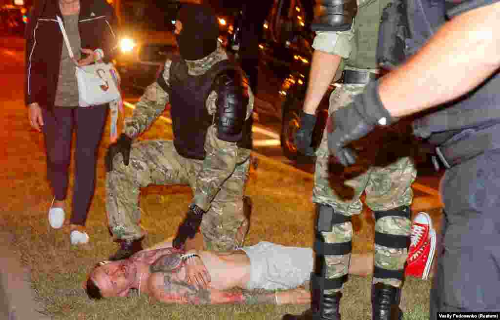 Minsk, Belarus - A law enforcement officer kneels next to a man laying on the ground during clashes with opposition supporters after polls closed at the presidential electio